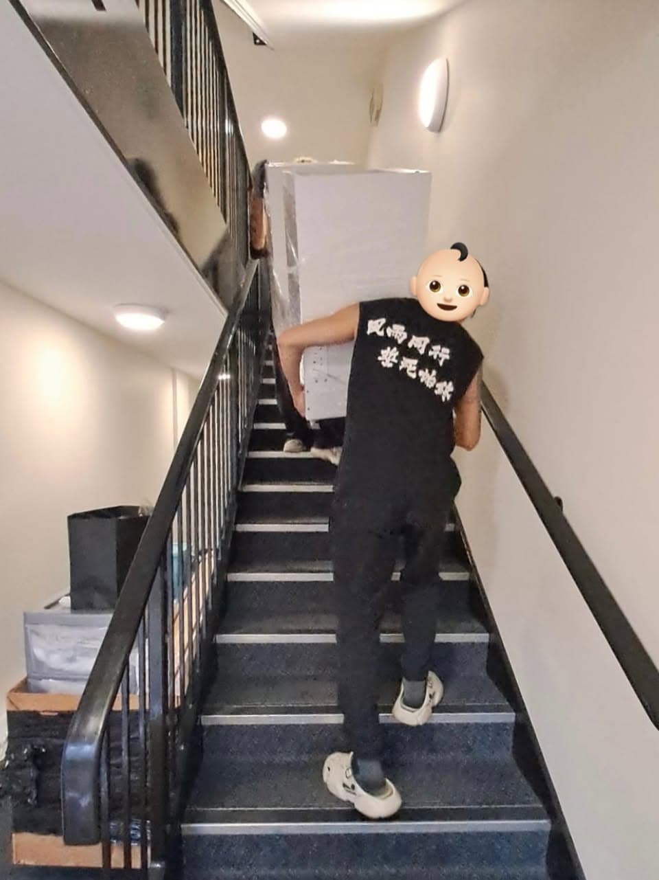 Crew carrying a large wrapped item on a staircase, with a face covered by an emoji in the original photo