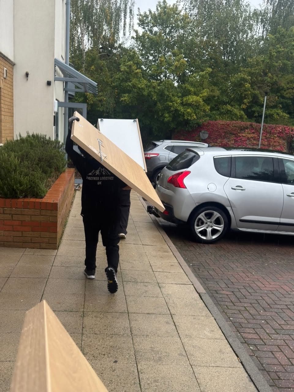 Two crew members carrying a large panel outside, with Together Logistics UK visible on a shirt