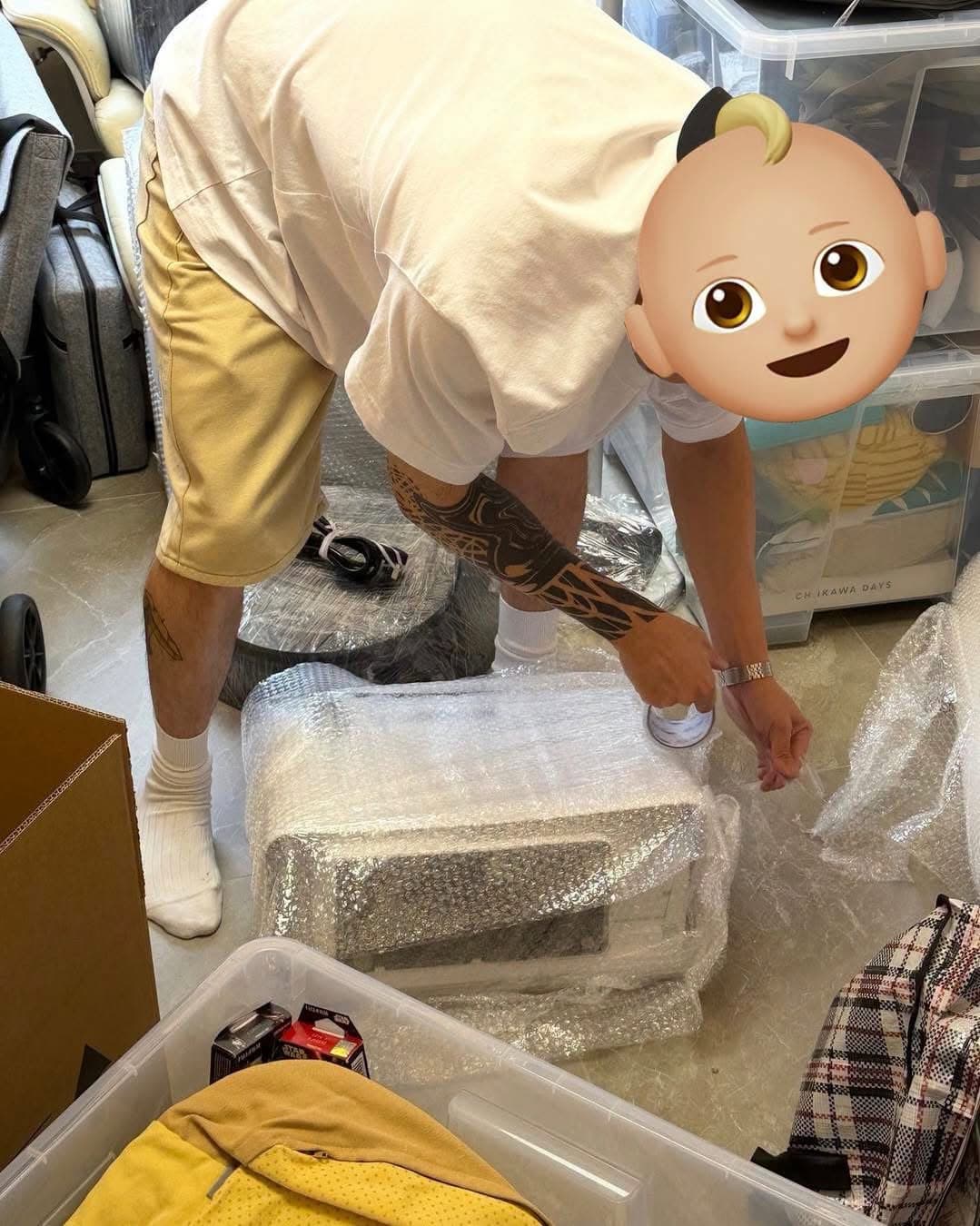 A team member wrapping a small appliance in bubble wrap, with a face masked by an emoji in the original photo